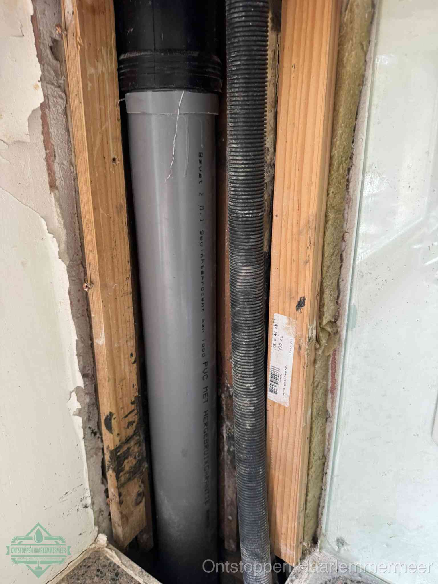 Een grijze PVC-afvoerbuis met een flexibele ribbelslang in een open wandconstructie, een verwaarloosde afvoer die te lang is blijven zitten in Haarlemmermeer