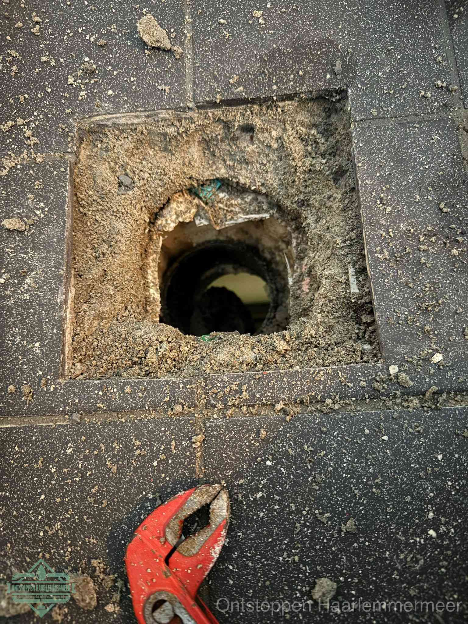 Een geopend rioolputje in een betontegelvloer met losgemaakt rooster en een zichtbare ronde afvoerbuis, het achterhalen waar de afvoerverstopping zit in Haarlemmermeer
