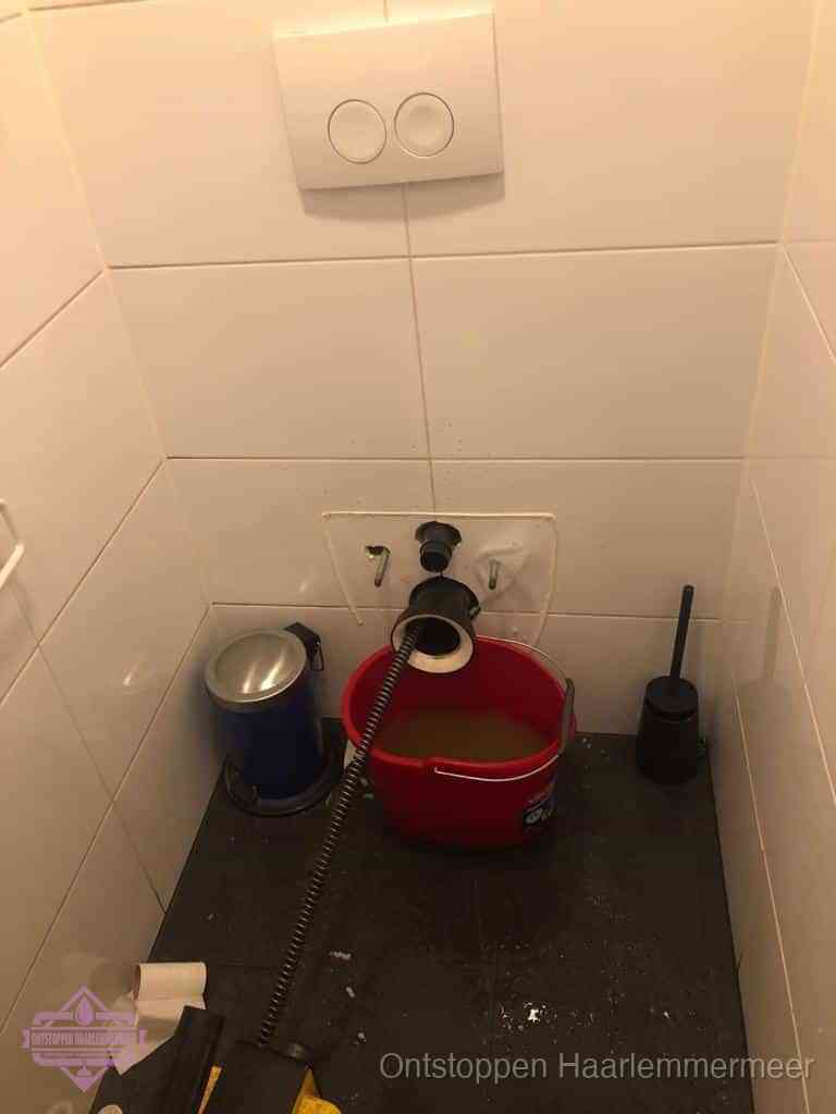 Een ontstopte wand-wc met verwijderde toiletpot waar een ontstoppingsveer in de wanduitgang verdwijnt, het achterhalen waar de verstopping zit in Haarlemmermeer