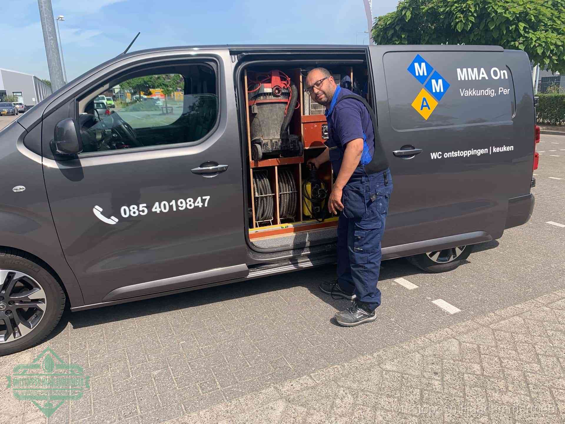 Een monteur bij de open schuifdeur van zijn bedrijfsbus op een parkeerplaats, klaar om de oorzaak van terugkerende afvoerverstoppingen aan te pakken in Haarlemmermeer