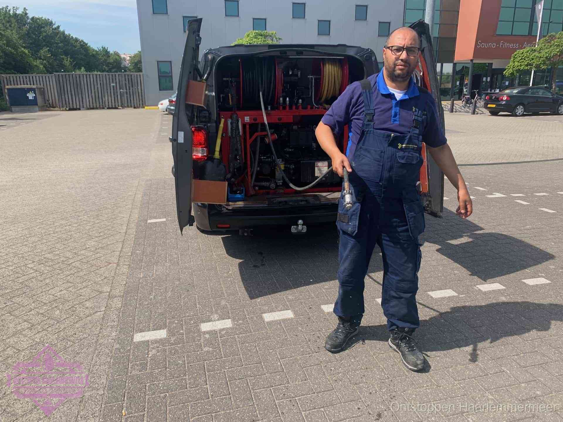 Een monteur bij zijn bestelbus met een hogedruk- en rioolreinigingsunit, klaar om de oorzaak van terugkerende wc-verstoppingen aan te pakken in Haarlemmermeer