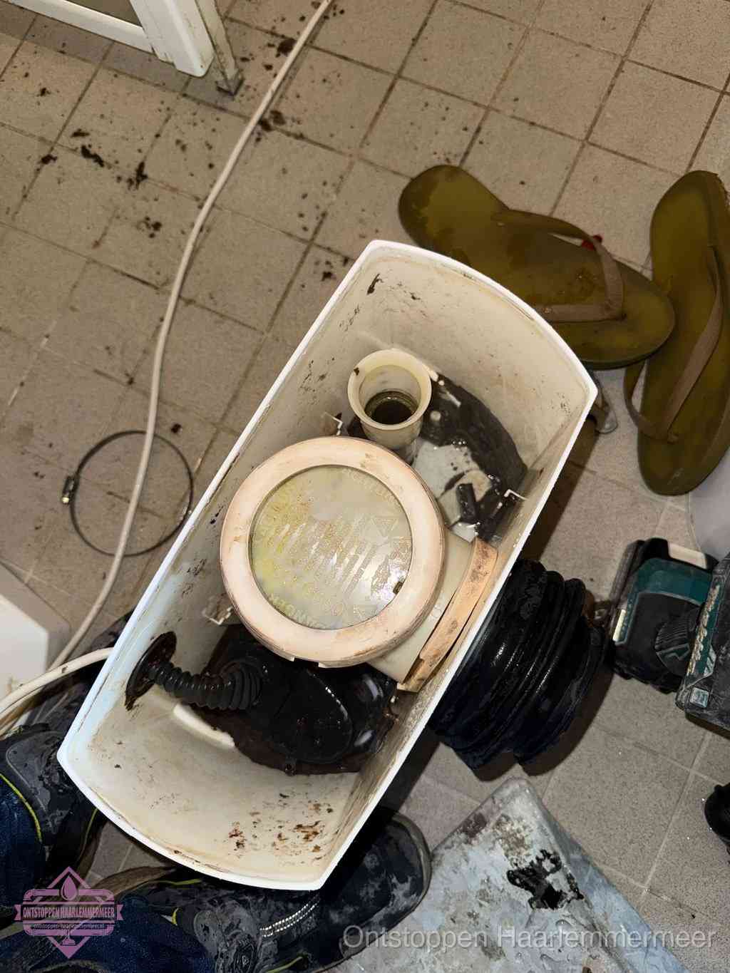 Een gedemonteerde toiletpot op de vloer met ontstoppingsveer en gereedschap ernaast, het verwijderen van een vastzittend voorwerp uit de wc in Haarlemmermeer