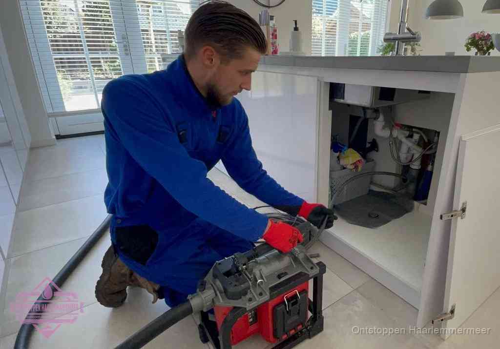 Een monteur voert een professionele elektrische ontstoppingsmachine in de afvoer onder de spoelbak tijdens het gootsteen ontstoppen in Haarlemmermeer