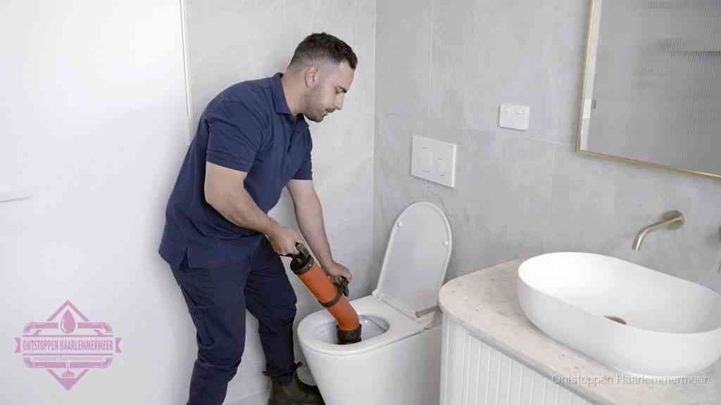Een man gebruikt een handmatige luchtdruk-ontstopper in een modern betegeld toilet om zelf de wc te ontstoppen in Haarlemmermeer